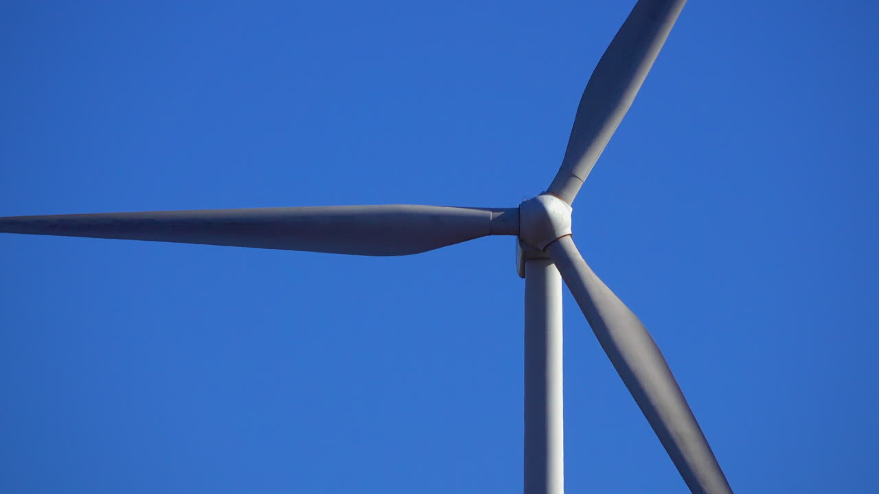 깊고 푸른 하늘을 배경으로 회전하는 풍력 터빈의 근접 망원 보기