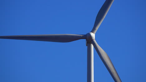 close-up telephoto view of a wind turbine spinning against a deep blue sky