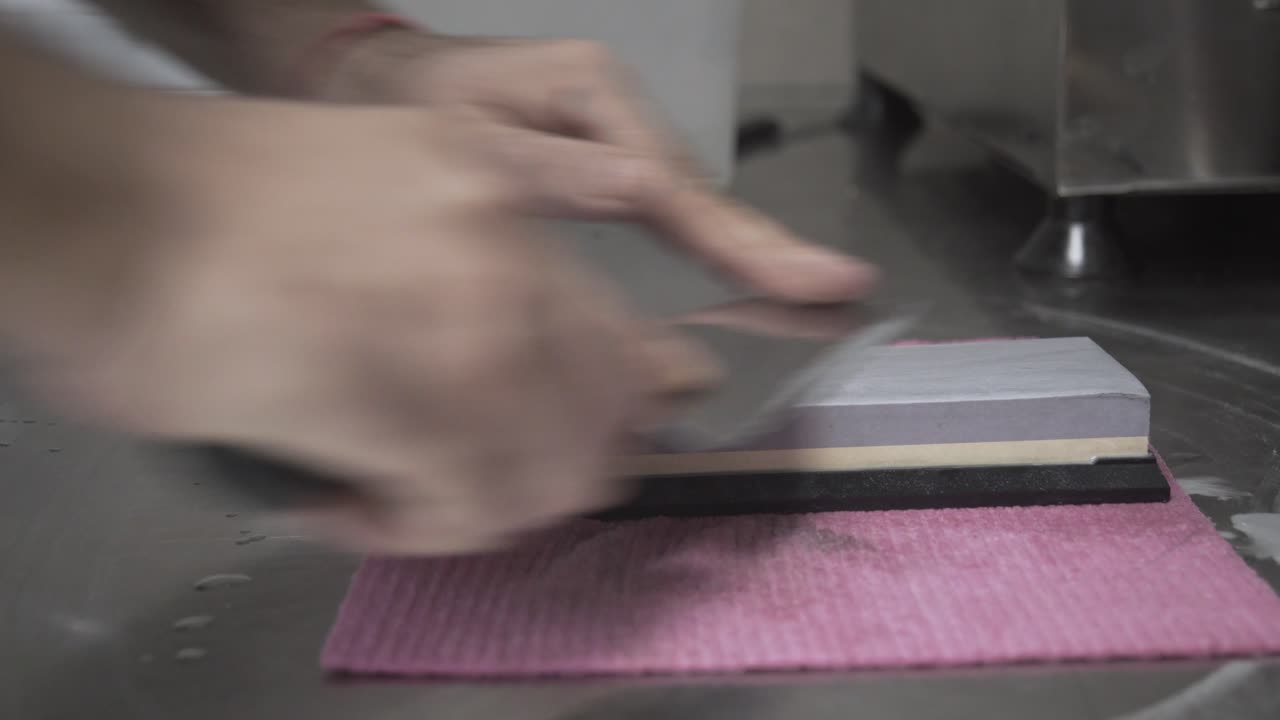 Nærbillede fra siden af kok der sliber en kniv med en slibesten 4K