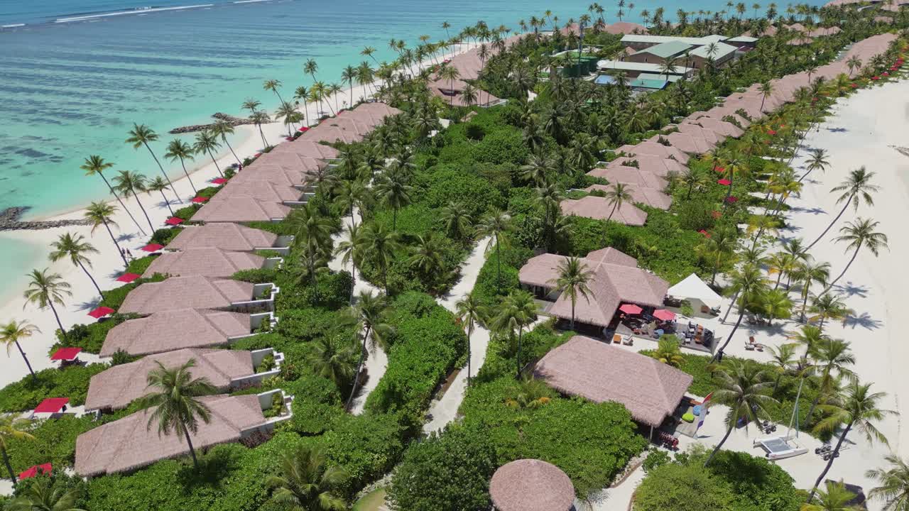 Beach resort with palm trees, thatched roof villas, white sand beach, exotic destination, Maldives. Aerial drone ascending