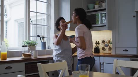 mixed race lesbian couple hugging and drinking coffee in kitchen