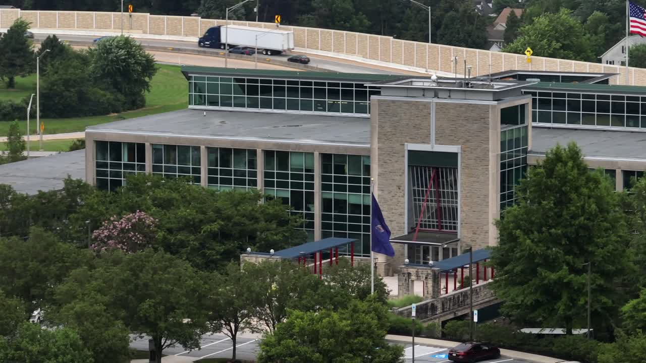 Aerial view of Pennsylvania turnpike commission office building in Harrisburg. Waving flags of American and Pennsylvania. Driving cars in background