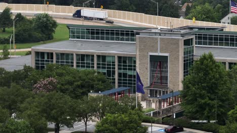 aerial view of pennsylvania turnpike commission office building in harrisburg. waving flags of american and pennsylvania. driving cars in background