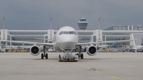wide shot of an airplane at push back. small truck pushing the plane back and turning it. buses driving in front of the plane. tower and dark clouds in the background.