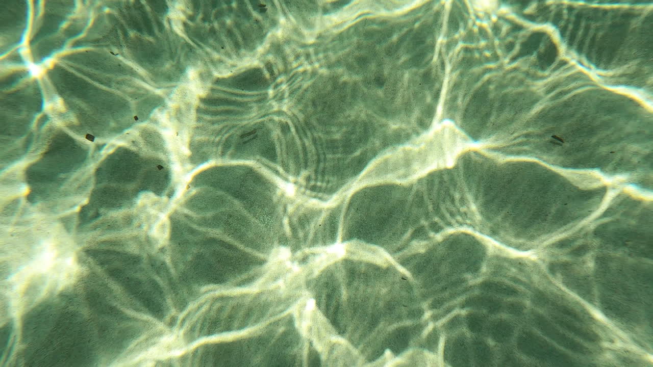 Mesmerizing underwater shot of sun light dancing on a sandy sea bed, creating beautiful caustic patterns. Ideal for nature documentaries, relaxation videos, and travel content
