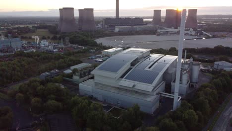 Aerial-view-descends-above-smart-solar-rooftop-factory-with-sunrise-emerging-from-behind-fossil-fuel-power-station