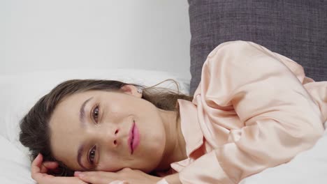 portrait of a beautiful woman in pink pajamas lying on the bed in the morning and thinking