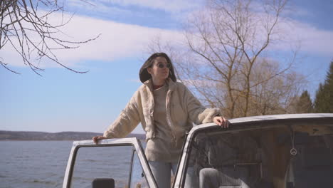 a young beautiful brunett girl with sunglasses looks out of the window of a van beside a lake