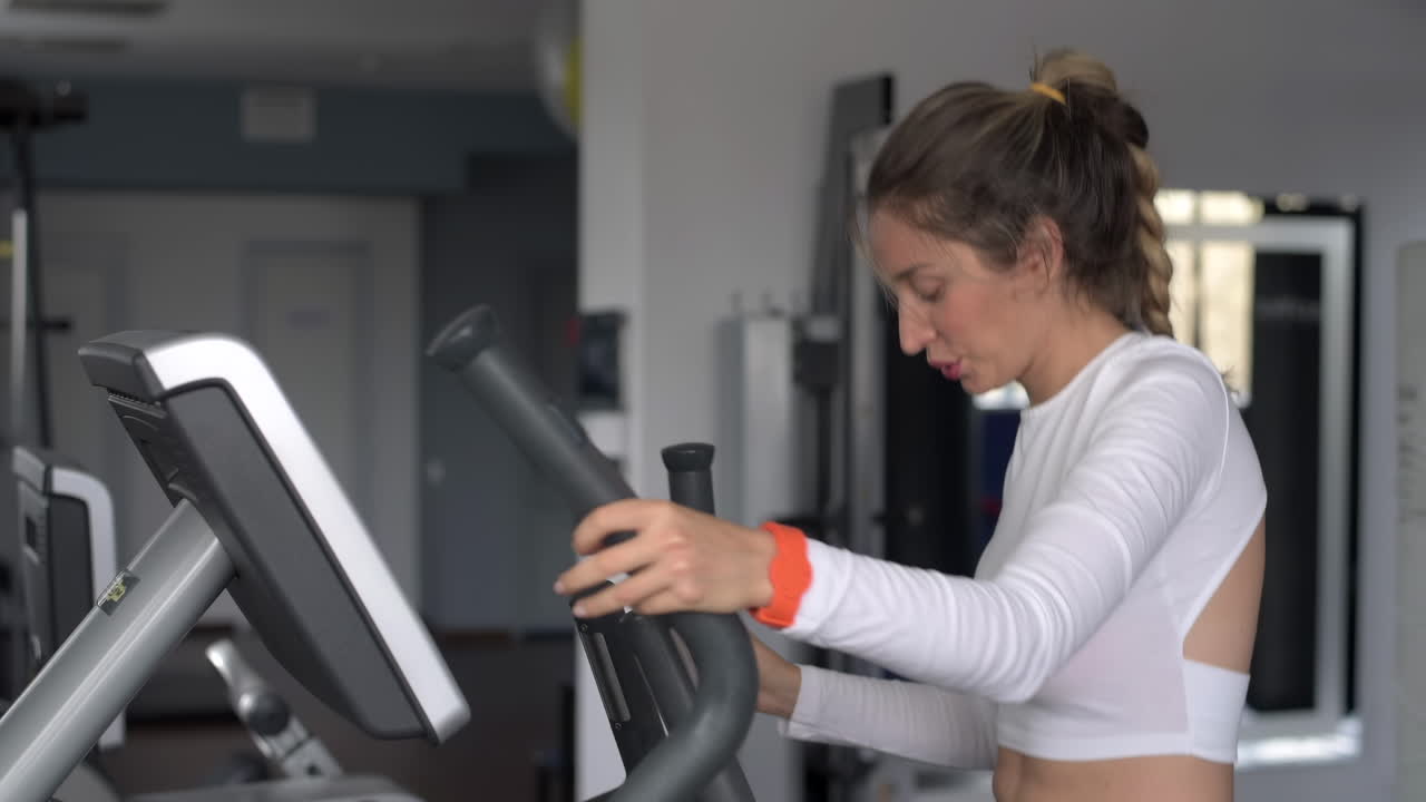 Woman in white activewear working out on the elliptical machine at the gym