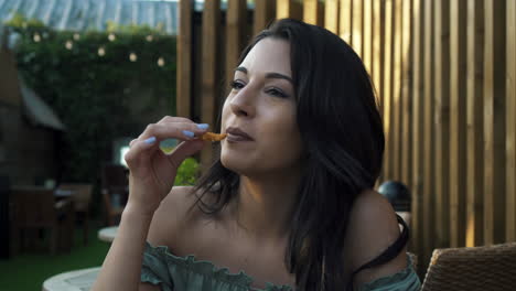 Adorable-woman-eating-curly-fries-in-a-cafe-in-London,-hispanic-latina-millennial-at-the-table-in-a-casual-outfit,-eating-and-having-fun,-smiling-and-enjoying-the-fast-food