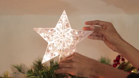 putting star decoration with flashing led lights on christmas tree top