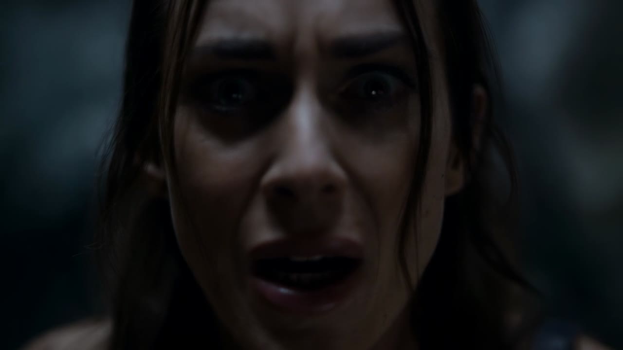 Exibindo uma mulher começando com uma expressão de surpresa, intensificando-se para uma careta em um cômodo escuro, com lágrimas