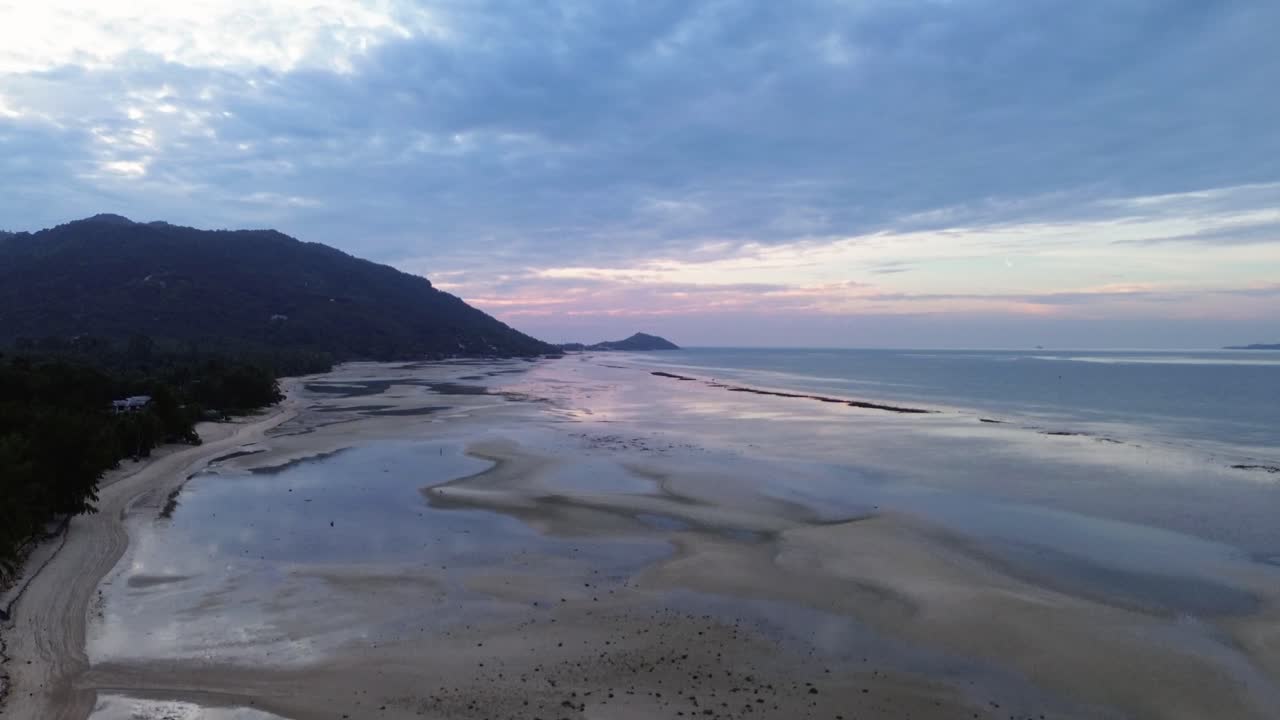 Beautiful aerial drone footage of sunrise over Koh Phangan, Thailand, featuring a pink horizon, calm sea, tropical coastline, and scenic island landscape in morning light