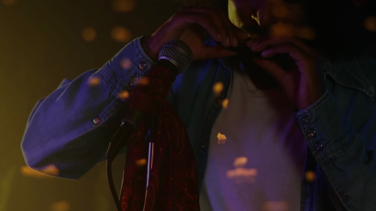 Male musician cupping harp, playing into mic on dim stage, embers layering over performer