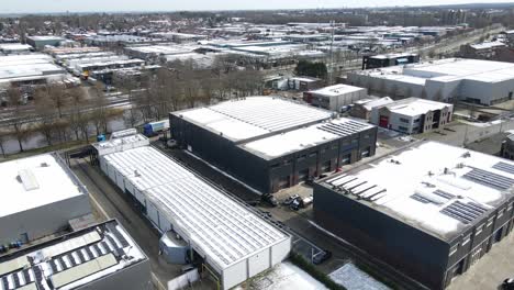 Aerial of large industrial zone with snow covered photovoltaic solar panels on rooftops in winter