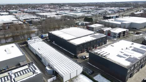 aerial of large industrial zone with snow covered photovoltaic solar panels on rooftops in winter