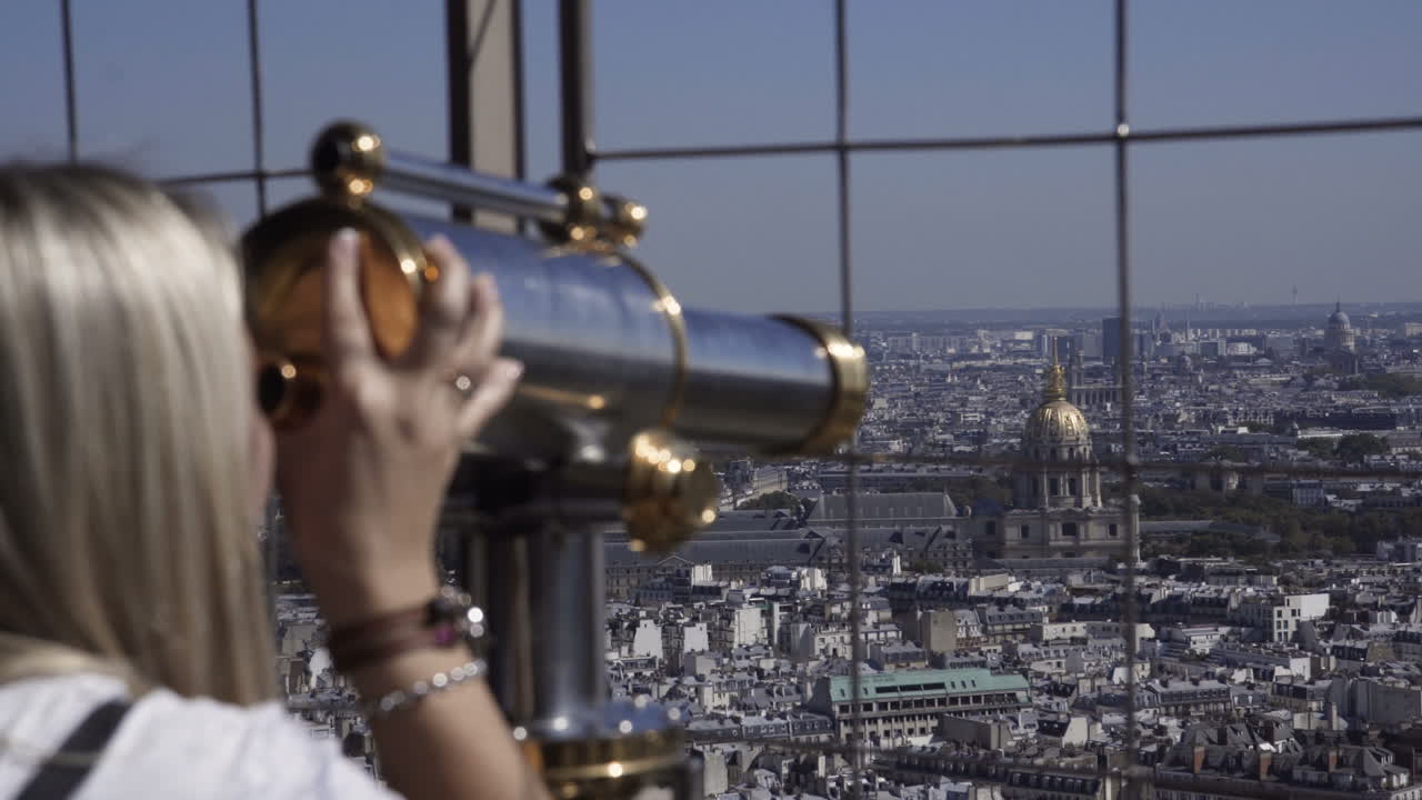 Woman using telescope at the Eiffel Tower looking at the Paris Cityscape