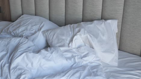 messy bed with white sheets and gray headboard