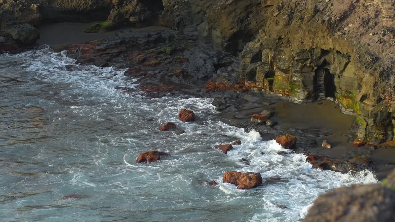 las olas espumosas ruedan sobre la playa y las piedras cerca del acantilado rocoso en tenerife