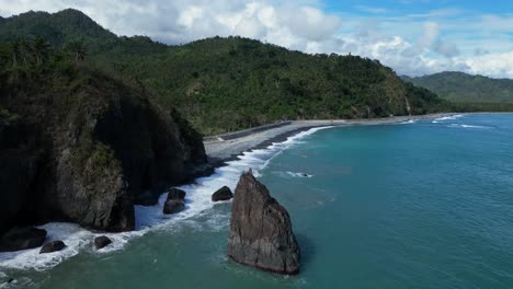 a drone shot captures a small mountain beside the ocean, with its rocky surface meeting the calm waves, creating a peaceful and stunning coastal scene.