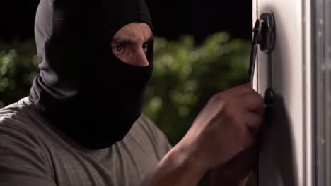 a suspenseful encounter: a heavily masked intruder attempts to break into a house under the veil of darkness, highlighting the perils of home security and vigilance