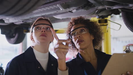 female tutor with student looking underneath car on hydraulic ramp on auto mechanic course