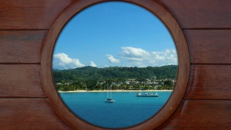 looking outside through a porthole of a cruise ship to the beach