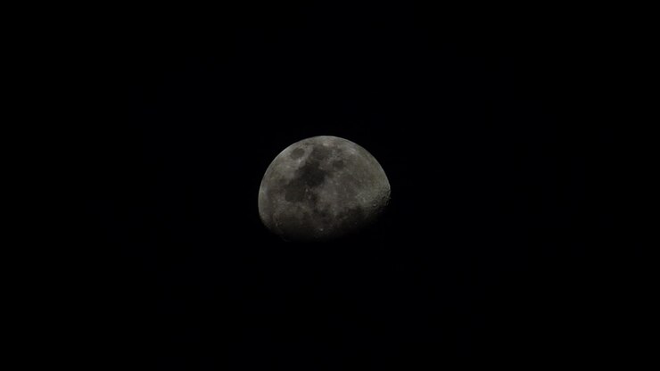 Lua gibosa minguante ascendendo em um céu escuro com nuvens finas passando.