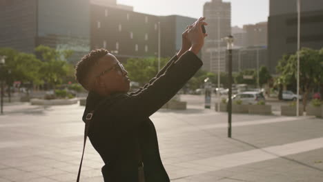 retrato de un hombre afroamericano de moda estudiante tomando una foto de la ciudad urbana usando tecnología de video de teléfono inteligente feliz disfrutando de viajes turísticos