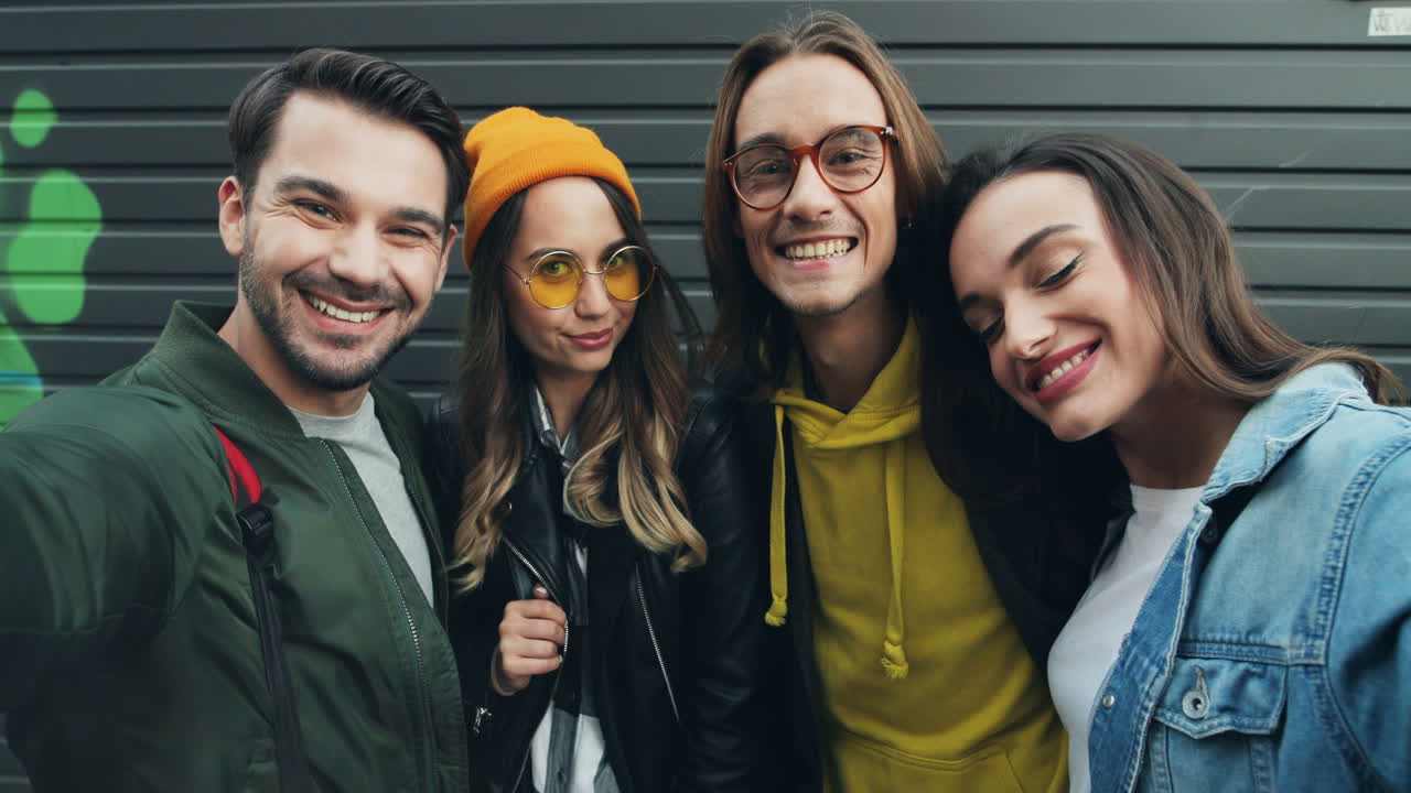 vista de cerca de un grupo de amigos caucásicos divertidos al estilo hipster sonriendo y posando mientras se toman selfies en la calle