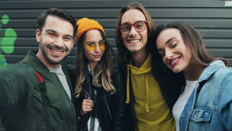 close-up view of group of caucasian funny friends in hipster style smiling and posing while taking selfies in the street