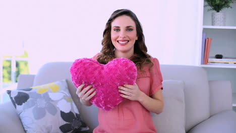 bonita modelo embarazada sentada en su sofá abrazando una almohada de corazón
