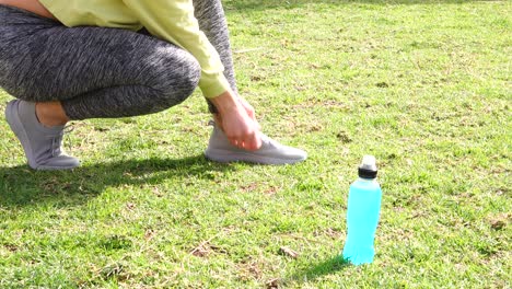 atleta atando zapatillas sobre césped con bebida isotónica al lado