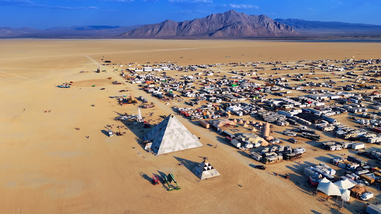 Desert camp below rugged mountain ridge. Camps, tents and vehicles stretch toward the mountains across the vast sandy plain