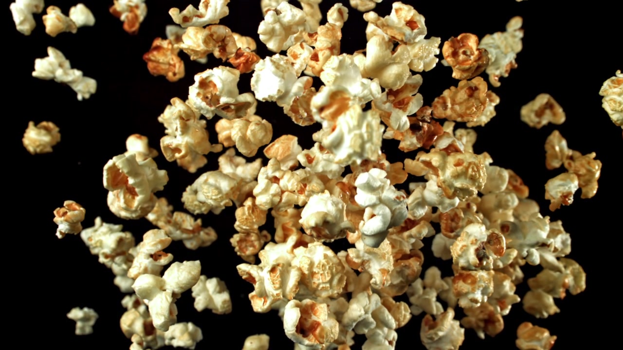 Chicchi di popcorn deliziosi che cadono al rallentatore su sfondo nero