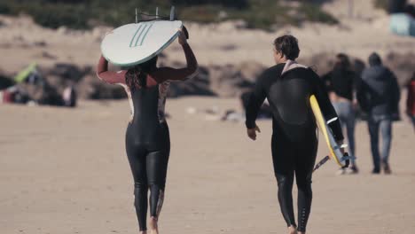 two surfers carrying surfboards and walking away from sand beach, back closeup view