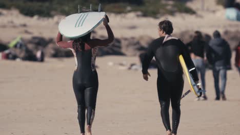 dos surfistas que llevan tablas de surf y se alejan de la playa de arena, vista de cierre posterior