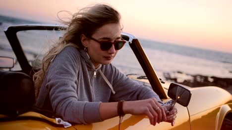 woman relaxing in convertible car and holding sparklers at sunset