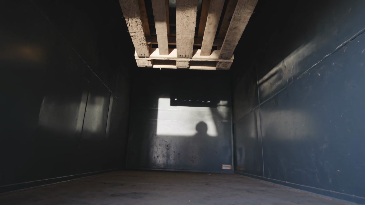 Raising arm loader shadow signaling guiding wooden pallet lowering in cargo box, rear light patch