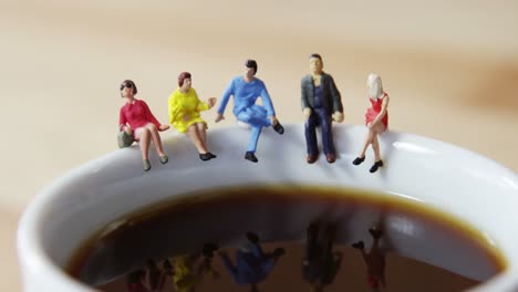 Gente-De-Negocios-En-Miniatura-Sentada-En-El-Borde-De-La-Taza-De-Café