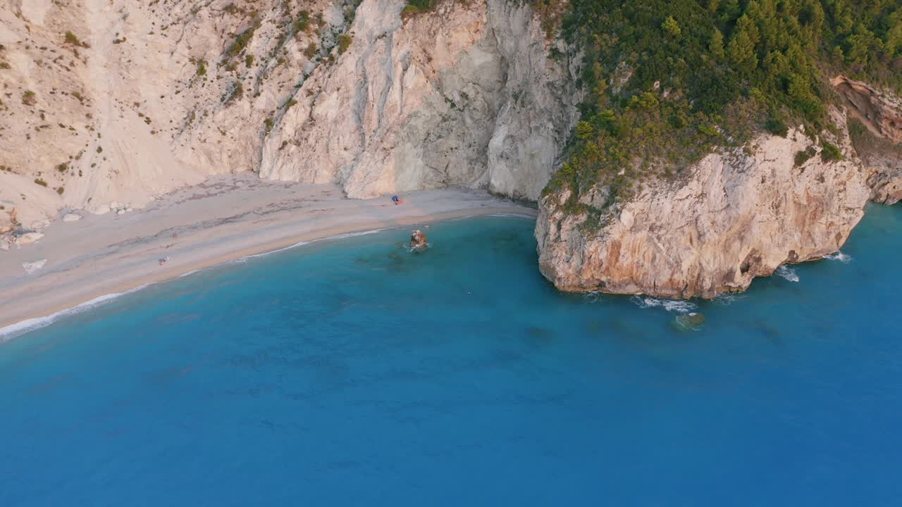 Aerial tilt down movement of beautiful Milos beach of Lefkada, Ionian island, Greece. Sunset golden sunlight on rocky cliffs surrounded by turquoise blue sea