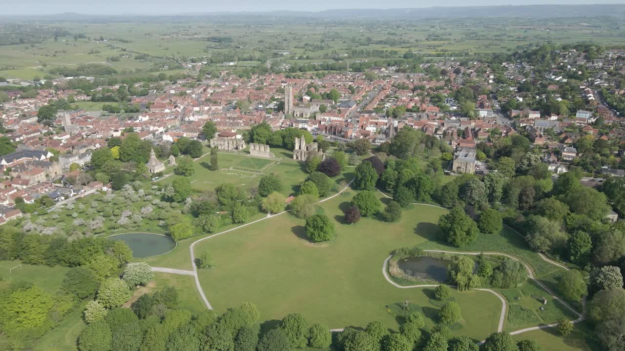 Aerial view of the Glastonbury Abbey ruins an 8th century monastery and gardens. Drone moving to the right showing the extension of the Glastonbury town and the ruins of the abbey. 4K, 60fps.