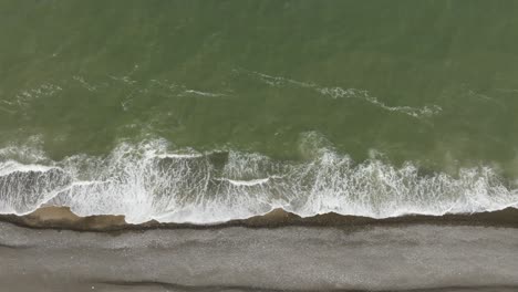 aerial view the green sea water washes the shore of the beach with many small pebbles