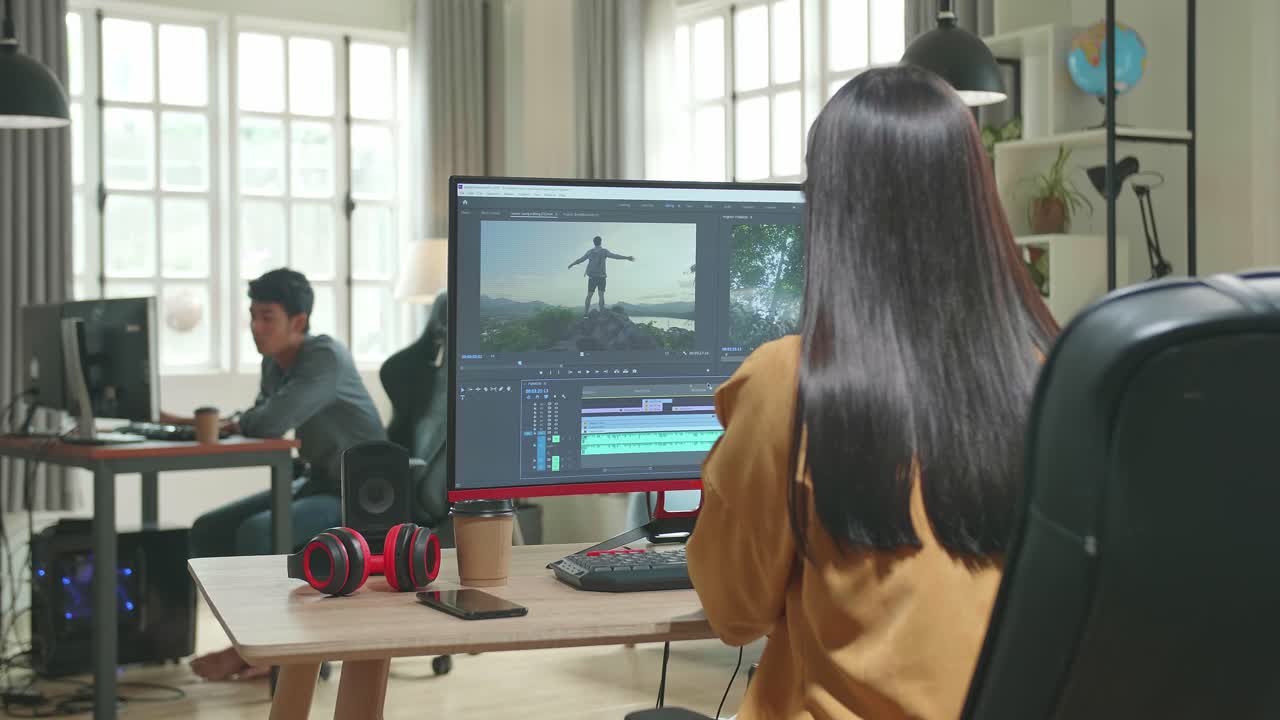 Back View Of Asian Female Video Editor Works With Footage And Sound On Her Personal Computer In Office