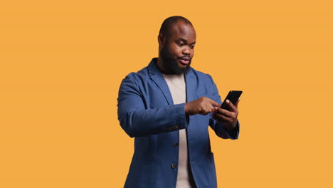 Portrait-of-energetic-happy-man-holding-phone-celebrating,-studio-background