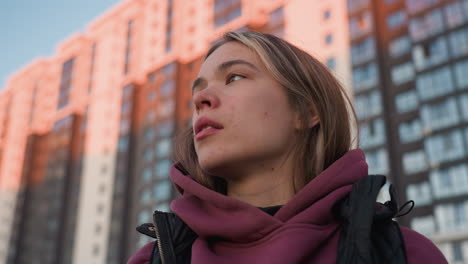 female instructor brushing strand of hair from face while exhaling relief after intense workout on urban sports court surrounded by tall residential towers at sunset with golden glow and candid focus