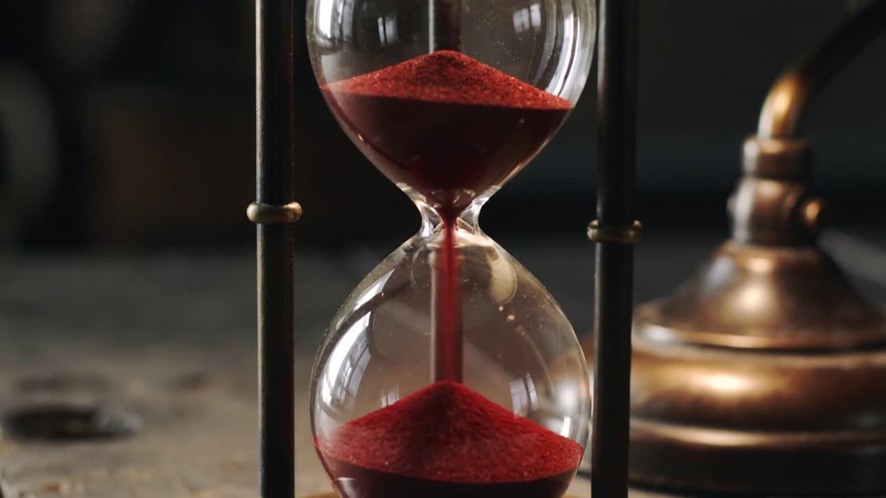 Starting stream, antique hourglass releasing red sand through neck at desk, timing with lamp