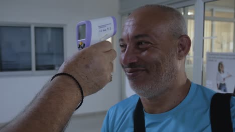 a un hombre se le revisa la temperatura con una pistola láser de temperatura infrarroja sin contacto en un puesto de control de viajes durante la pandemia de covid-19