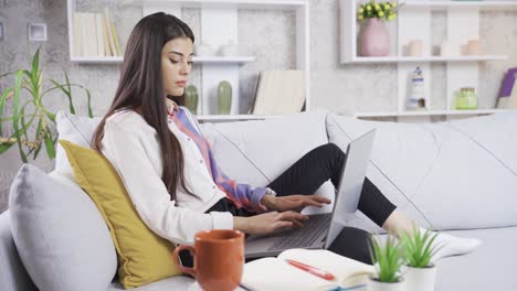 Beautiful-young-woman-sitting-on-sofa-at-home-and-working-on-laptop.