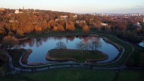 Schöne-Drohne-Erschossen-Menschen,-Die-Im-Städtischen-Park-Mit-Teich-In-England-Spazieren-Gehen